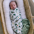 Newborn baby swaddled in a blanket with dinosaur pattern in a moses basket.