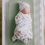 Newborn baby swaddled in a personalized swaddle blanket with name and animal patterns in a crib.