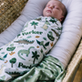 Newborn baby swaddled in a blanket with dinosaur patterns and 'Parker' printed on it, lying on a textured surface.