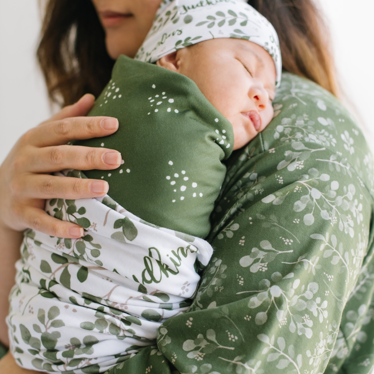 Mother holding a baby wrapped in a green and white floral-patterned swaddle wrap personalized with baby name.